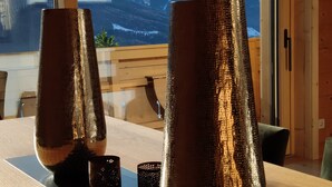 Una mesa de madera con dos jarrones metálicos y una vela, frente a una ventana con vistas a la montaña.