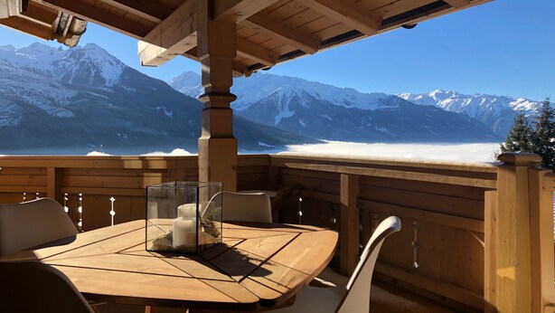 Una terraza de madera con una mesa y sillas, con vistas a montañas nevadas.