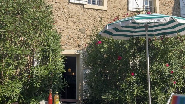A rustic stone building with a gravel patio, outdoor seating, and a striped umbrella. - Maison du Néflier (N°2) (Marcorignan)