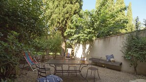 A patio with a round table and chairs, surrounded by greenery and a low wall. - Maison du Néflier (N°2) (Marcorignan)