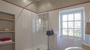 A bathroom with a glass-enclosed shower, a toilet, a window, and shelves with towels. - Maison du Néflier (N°2) (Marcorignan)