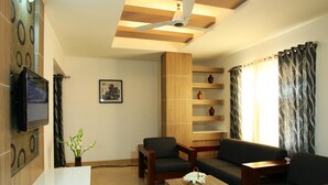 A living room with a TV, a sofa, a coffee table, a bookshelf, and a ceiling fan.