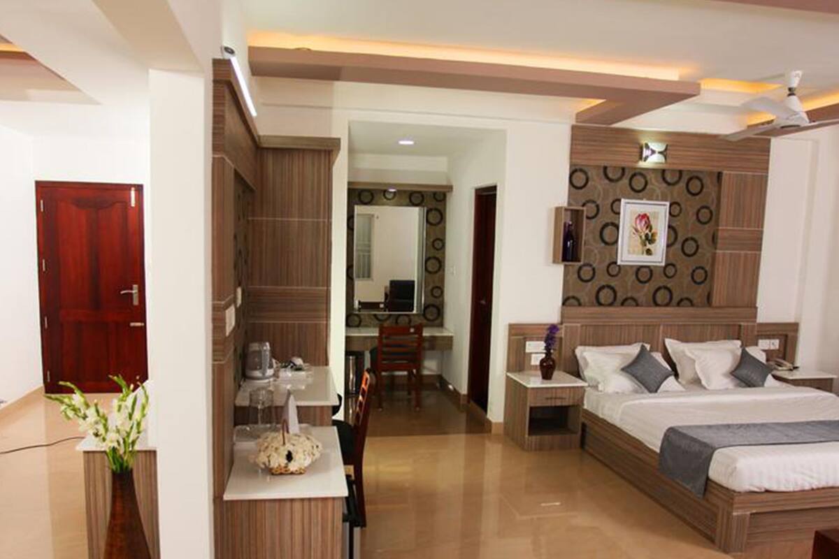 A modern hotel room with a wooden bed, a desk, and a small kitchenette.