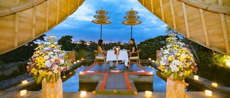 A romantic outdoor dining setup with a bamboo arch, a table with chairs, and flower arrangements.