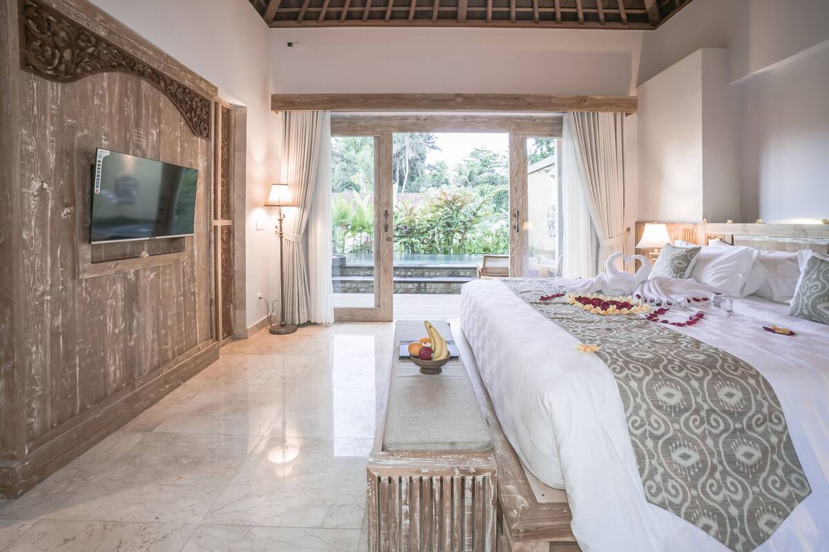 Un dormitorio espacioso con una cama grande, un televisor montado en un panel de madera y un balcón con vistas a la vegetación.