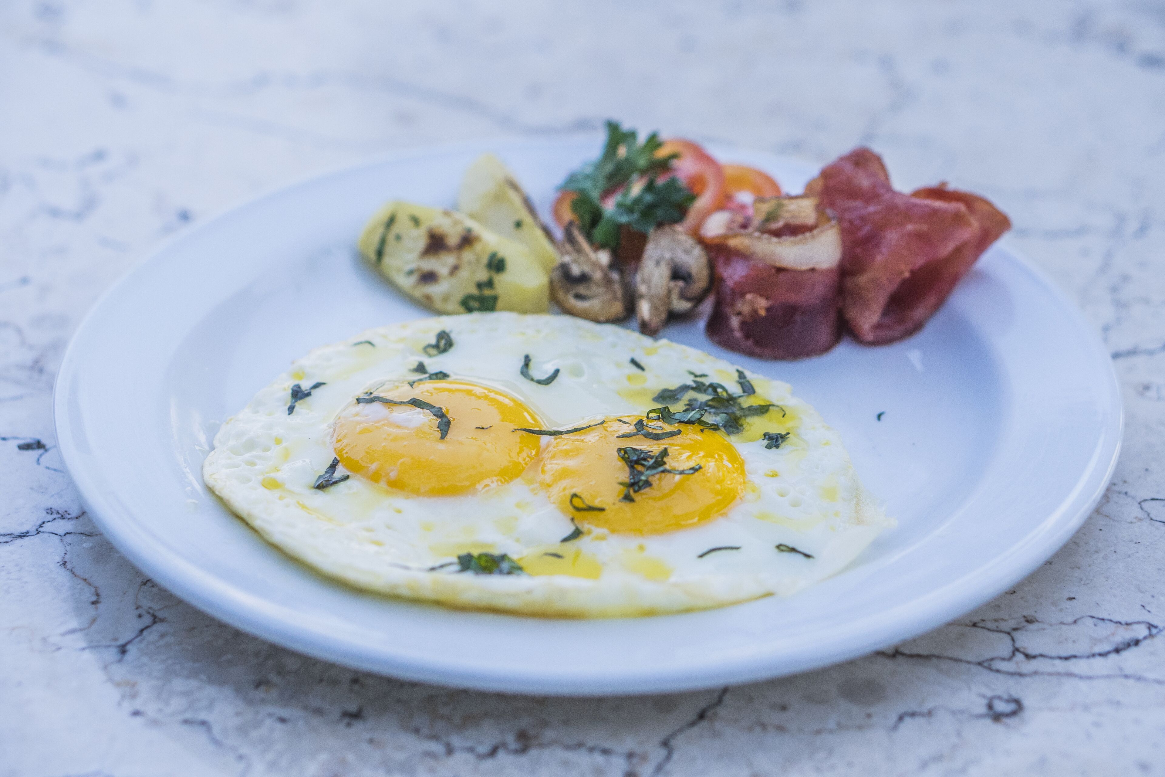 A plate with two sunny-side-up eggs, grilled vegetables, and bacon on a white plate.