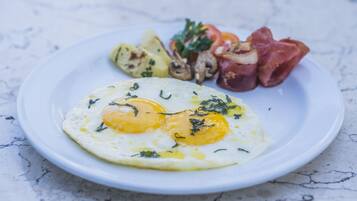 A plate with two sunny-side-up eggs, grilled vegetables, and bacon on a white plate.