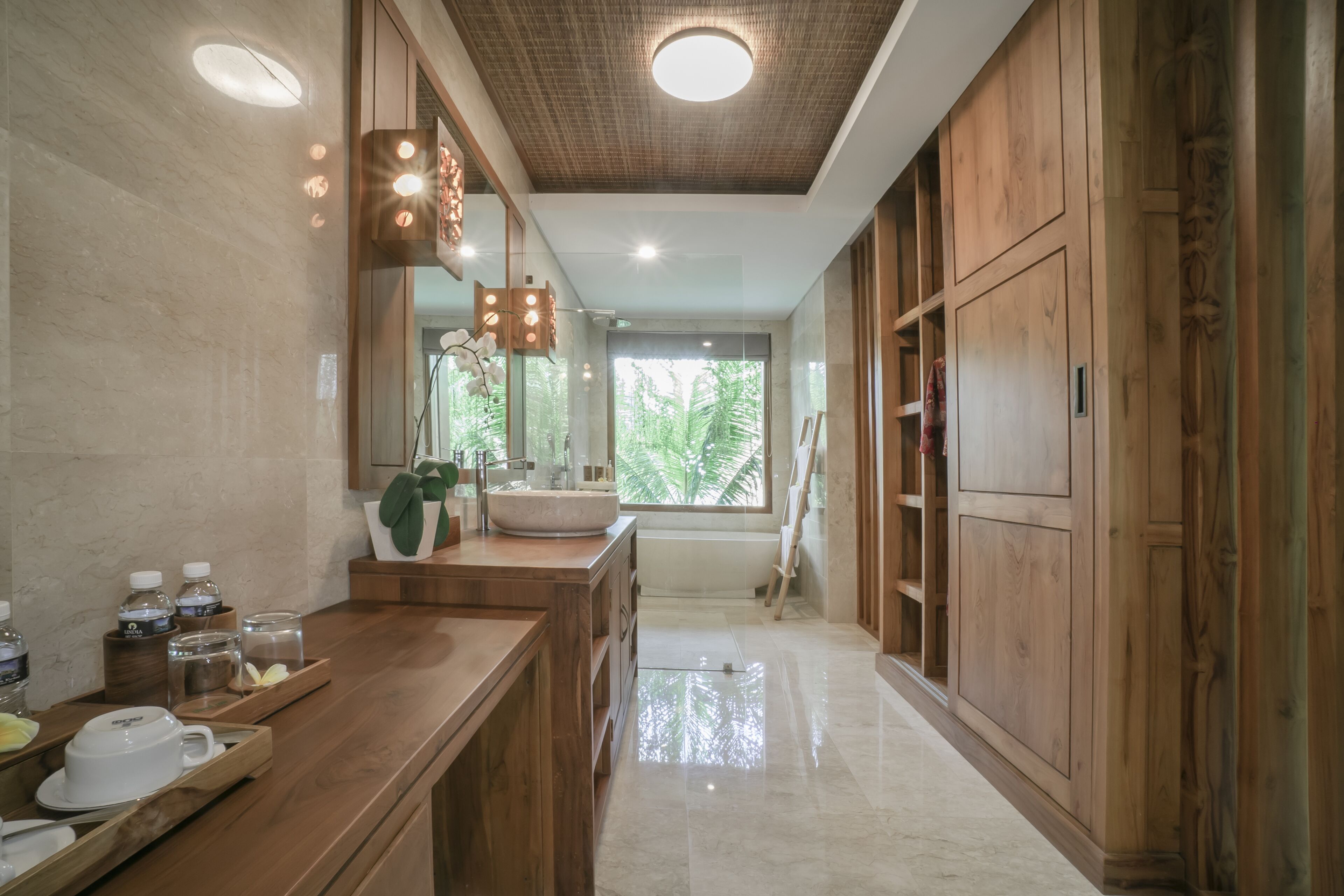 A modern bathroom with a wooden vanity, a large mirror, and a view of greenery outside.