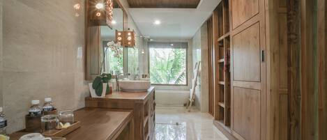 A modern bathroom with a wooden vanity, a large mirror, and a view of greenery outside.