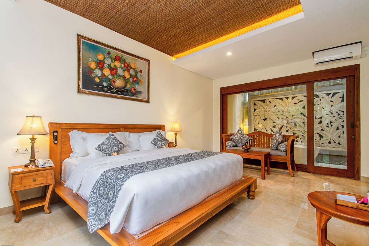 Un dormitorio amplio con una cama grande, cabecera de madera, dos mesitas de noche con lámparas, una silla de madera y un cuadro decorativo en la pared.