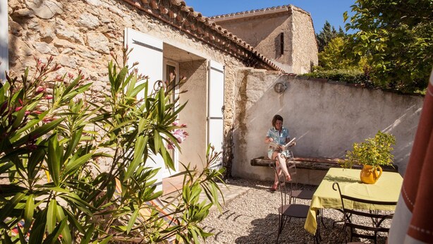 A stone building with a rustic exterior, a wooden bench, and a table with a yellow tablecloth. - Maison du Prunier (N°5) (Marcorignan)