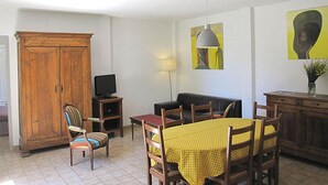 Un soggiorno con un armadio in legno, una televisione, un divano, un tavolo da pranzo con sedie e opere d'arte alle pareti.