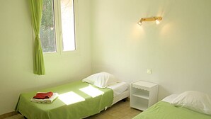 Una stanza piccola e pulita con due letti singoli, un comodino, una finestra con tende e un punto luce a parete.