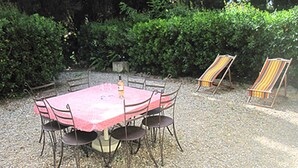 Un tavolo rotondo con sei sedie, una bottiglia e una sedia da spiaggia a righe in un giardino.