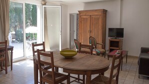 Zona pranzo con tavolo rotondo in legno, sedie, una ciotola verde, un televisore e un armadio.
