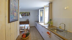 A kitchen with a wooden table, a bowl of vegetables, a sink, and a window. - Maison de l'Amandier (N°9) (Marcorignan)
