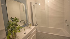 A bathroom with a white sink, mirror, and a shower area with a glass door. - Maison de l'Amandier (N°9) (Marcorignan)