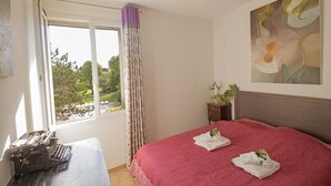 A bedroom with a large bed, a window with curtains, a ceiling fan, and a painting on the wall. - Maison de l'Amandier (N°9) (Marcorignan)