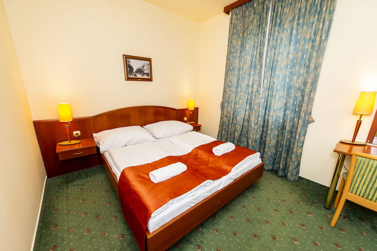 A hotel room with a wooden bed, two bedside tables with lamps, a green patterned carpet, and a blue curtain.