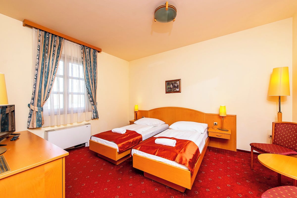 A hotel room with two beds, a desk, a chair, and a lamp.