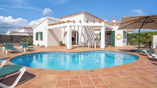 A swimming pool with lounge chairs and a pergola, surrounded by a white building with green shutters. - Beach Resort Villa with Private Pool and Air-conditioning (Cala en Porter, Alaior)