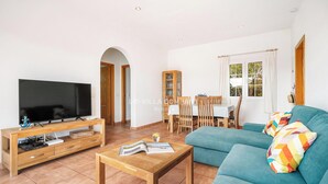 A living room with a TV, wooden furniture, a sofa, and a dining area with a table and chairs. - Beach Resort Villa with Private Pool and Air-conditioning (Cala en Porter, Alaior)