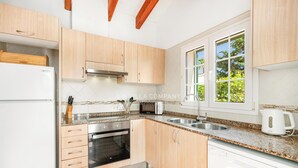 A modern kitchen with light wood cabinets, stainless steel appliances, a built-in oven, a microwave, and a double sink. - Beach Resort Villa with Private Pool and Air-conditioning (Cala en Porter, Alaior)