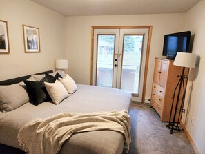 A bedroom with a bed, two bedside lamps, a television on a stand, and a wardrobe.