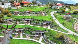 A rural village with traditional stone houses, winding paths, and a deer in the foreground. - Milyos Hotel (Bucak)