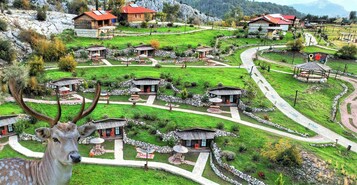 Un pueblo rural con casas de piedra tradicionales, senderos sinuosos y un ciervo en primer plano.