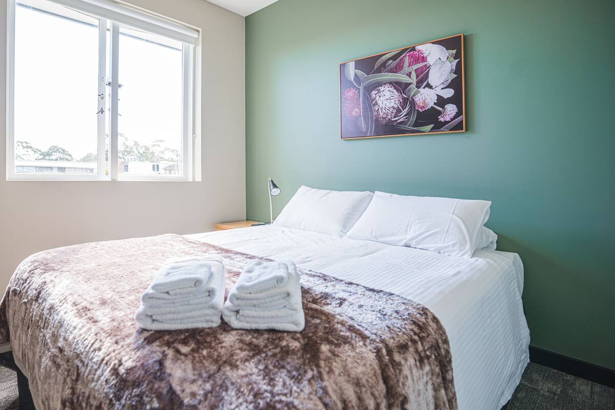 Una camera d'albergo con un letto, una finestra, un quadro e un comodino.