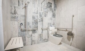A modern bathroom with a marble wall, a white toilet, and a shower with a handheld showerhead. - The Peakhurst (Peakhurst)