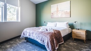 Quarto de hotel bem arrumado com uma cama, abajures, mesa de cabeceira e uma pintura de paisagem urbana na parede.
