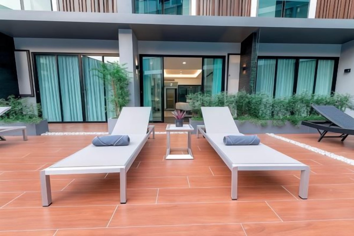 Una zona relax esterna moderna con due poltrone bianche, un tavolino con un vaso e una panca.