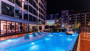 A swimming pool with lounge chairs, surrounded by a building with multiple floors and large windows.