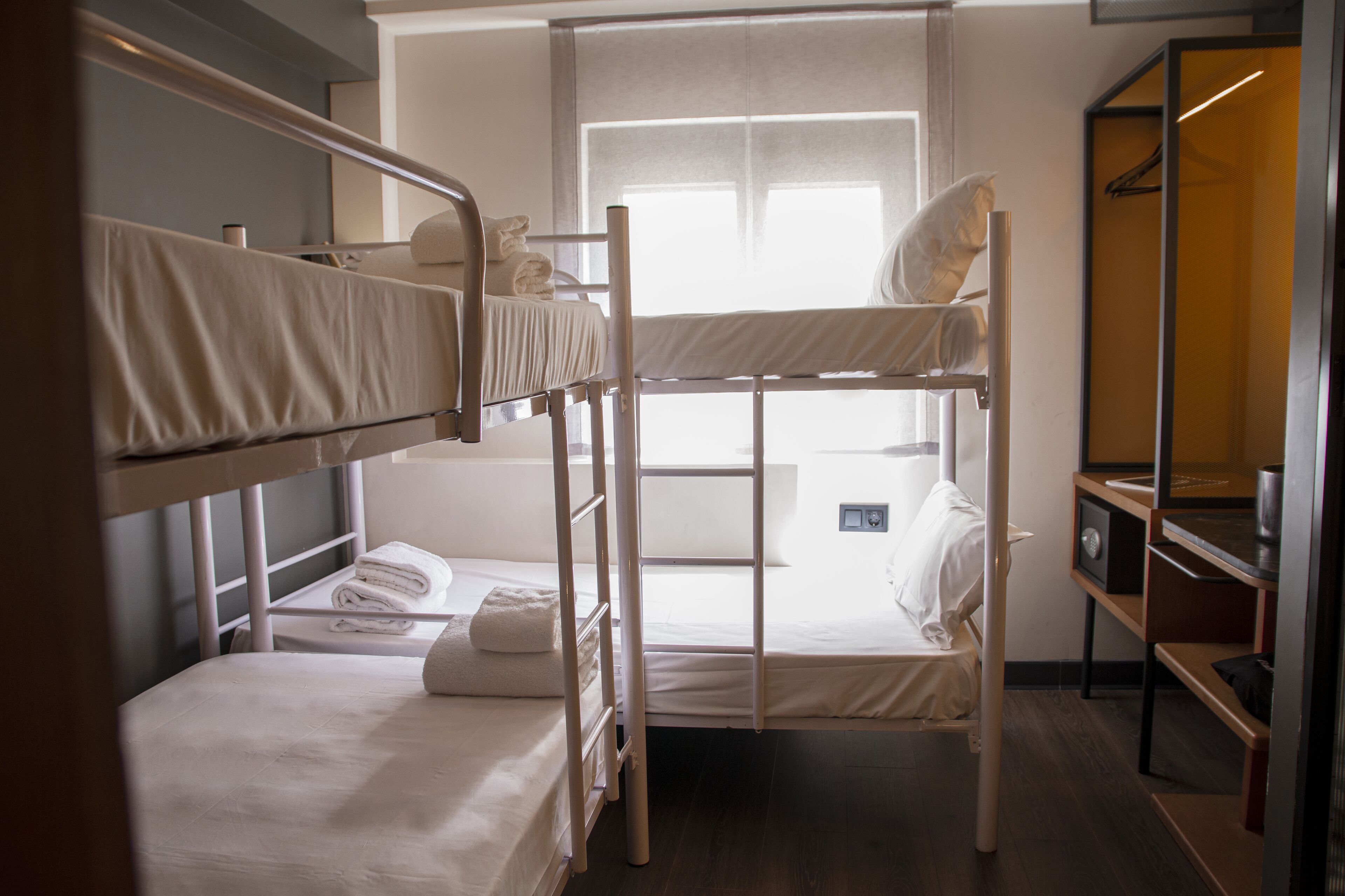 Une chambre avec un lit superposé, une fenêtre, une table de chevet et une armoire.
