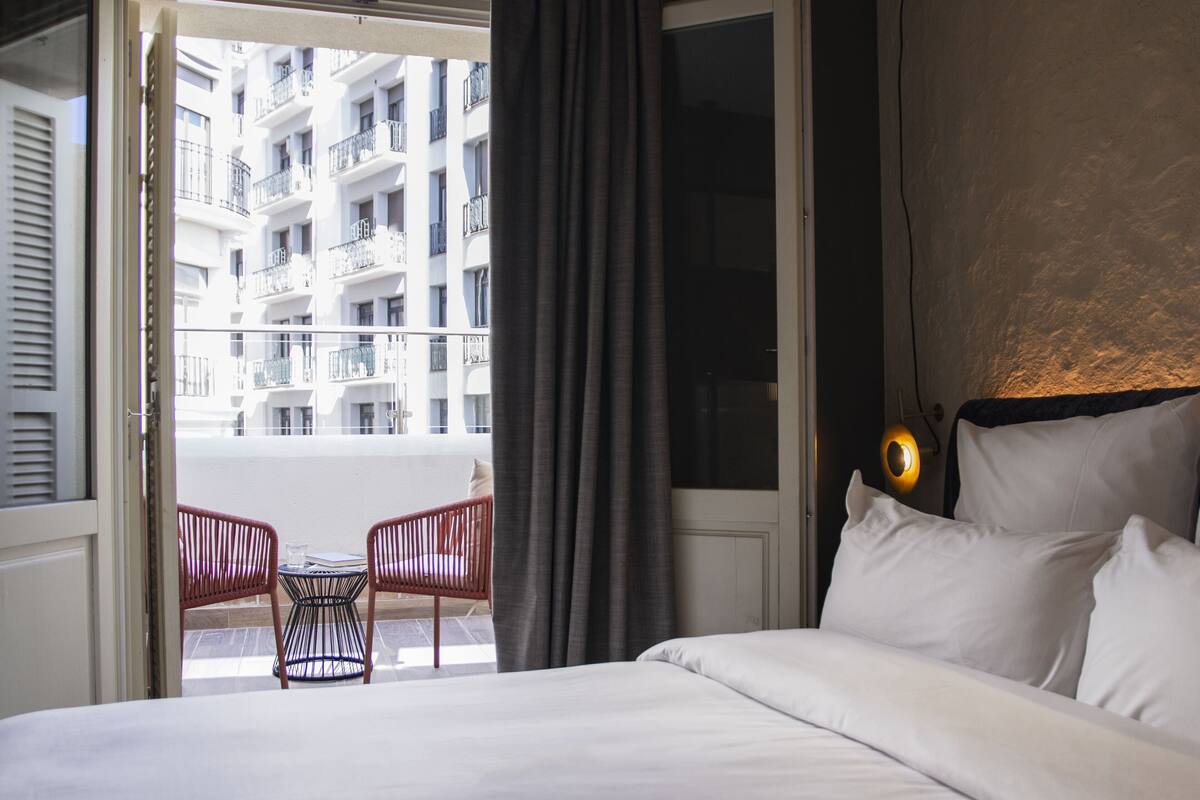 Une chambre d’hôtel avec un lit, une petite table, deux chaises et une vue sur un immeuble doté de balcons.