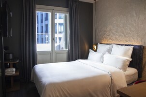 Hotellihuone, jossa on suuri sänky, yöpöytä, televisio ja ikkuna, jossa on verhot.