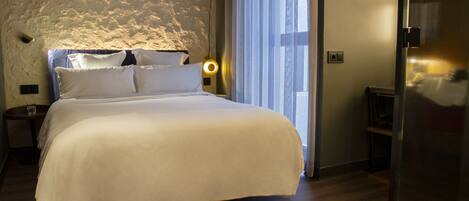 A neatly made bed with white linens in a room with wooden flooring and a textured wall.