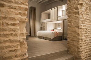 A bedroom with a bunk bed, a bedside table, and a window with curtains.
