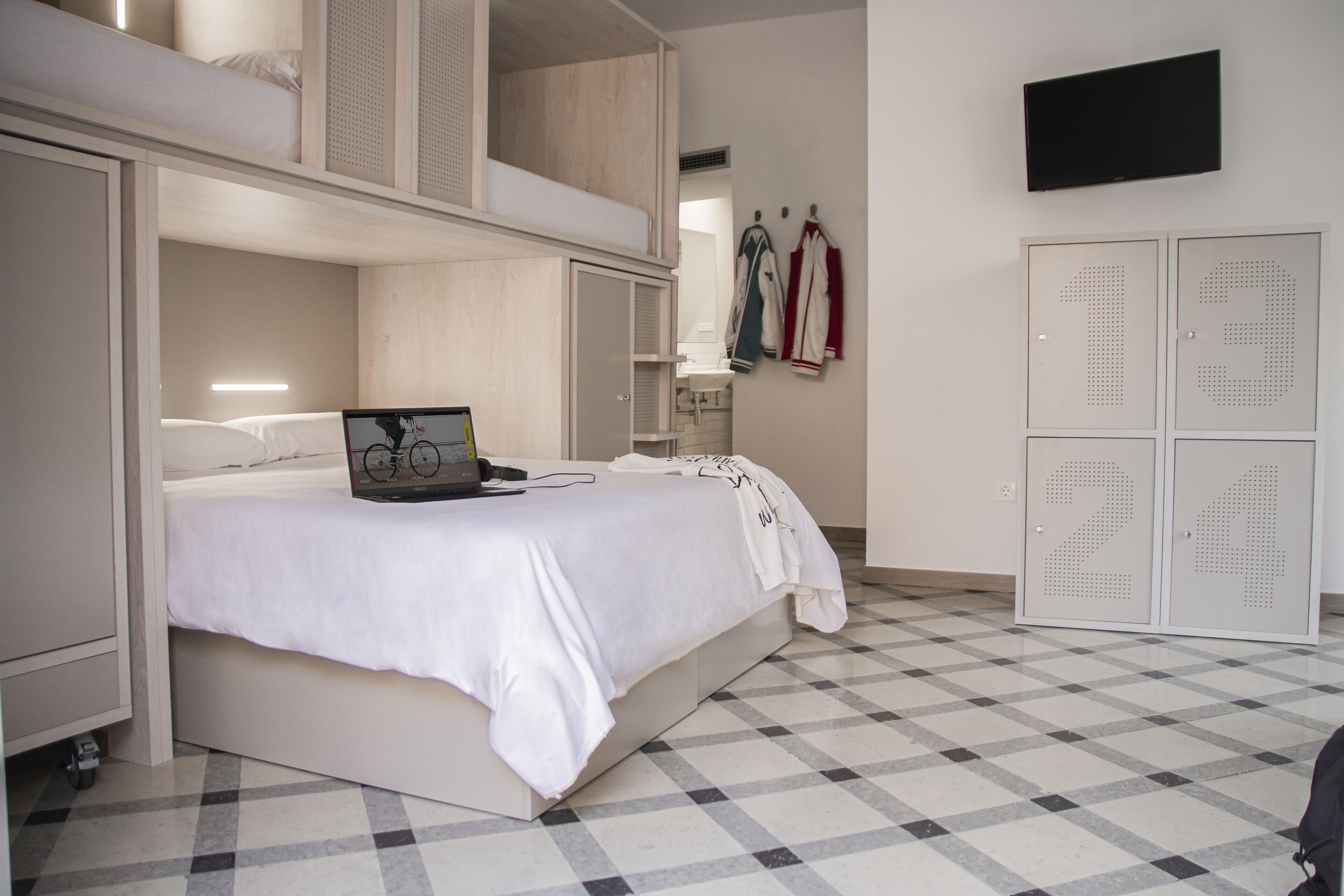 A room with a bunk bed, a desk with a laptop, a mirror, and a wardrobe with numbers on the doors.