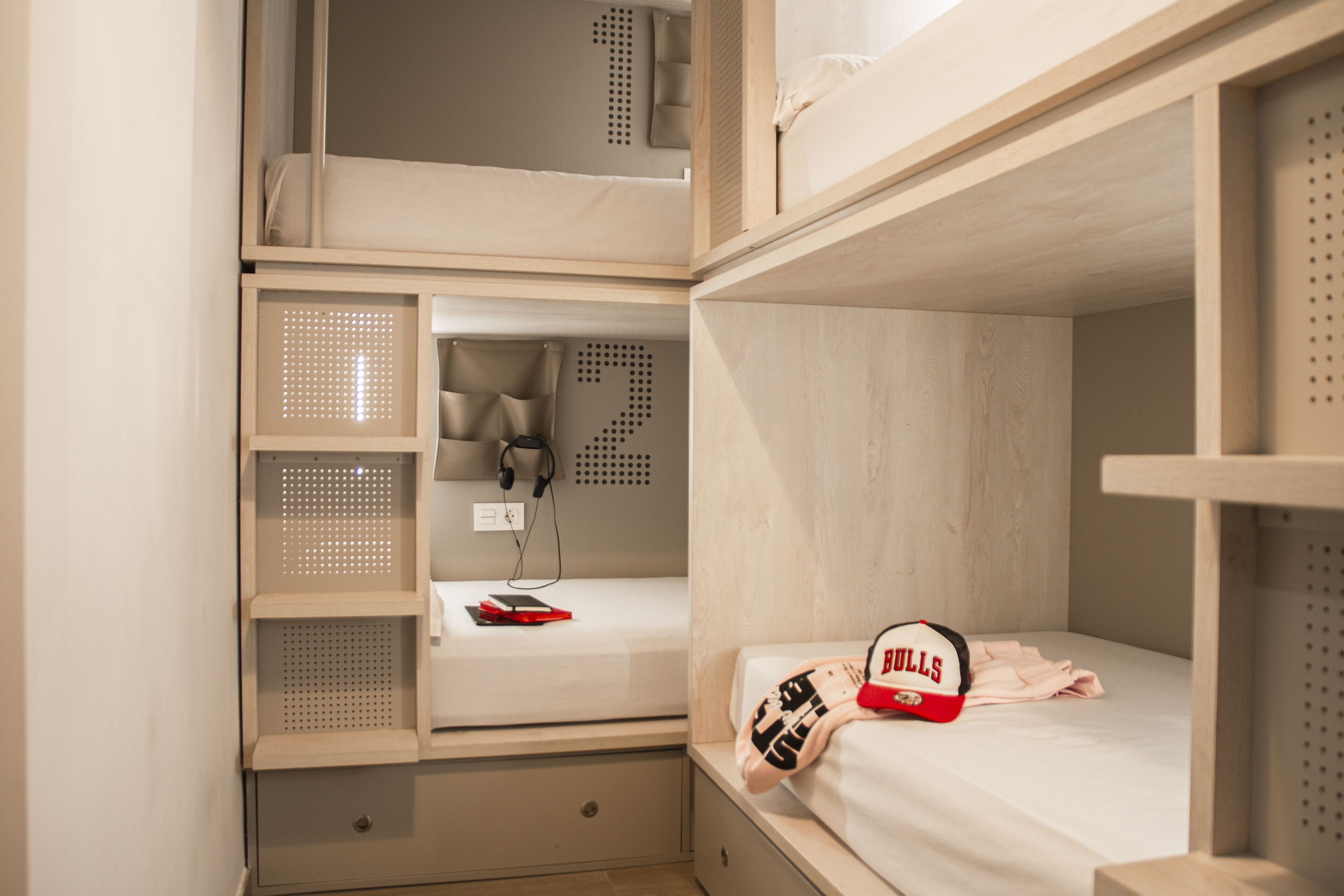 A bunk bed room with a desk, a lamp, and a cap on the bed.