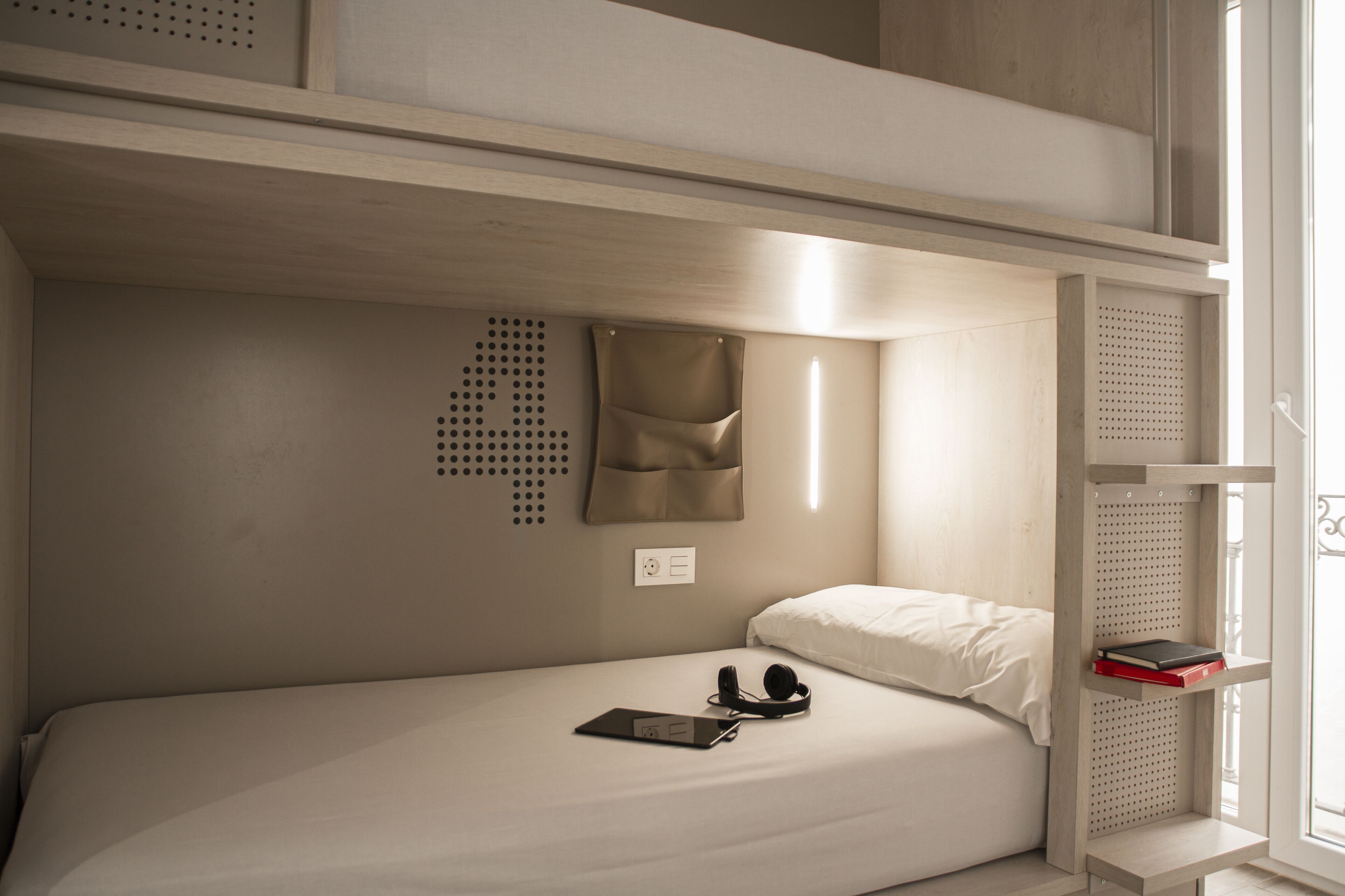 A bunk bed room with a white mattress, a pillow, a book, and headphones on the lower bunk.