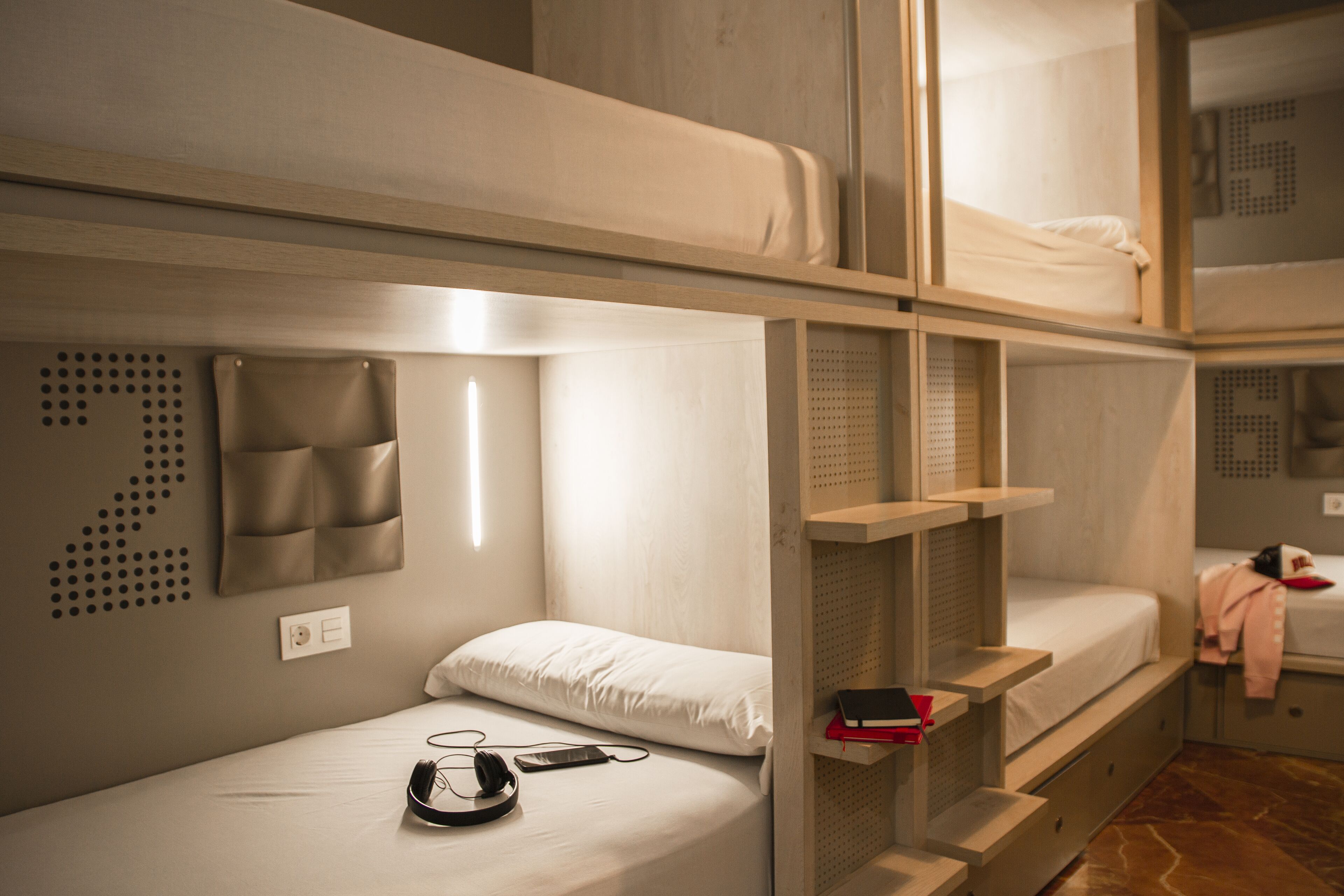 A bunk bed room with a small desk and shelves, a power outlet, and a wall-mounted storage unit.