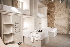 A modern, minimalist bedroom with bunk beds, built-in storage, and a stone wall. - Room Salvador (Seville)