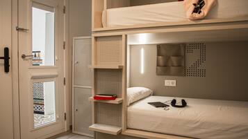 Habitación con literas, una ventana, una puerta y un estante pequeño con un libro.