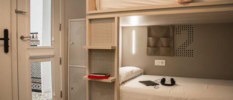 Habitación con literas, una ventana, una puerta y un estante pequeño con un libro.