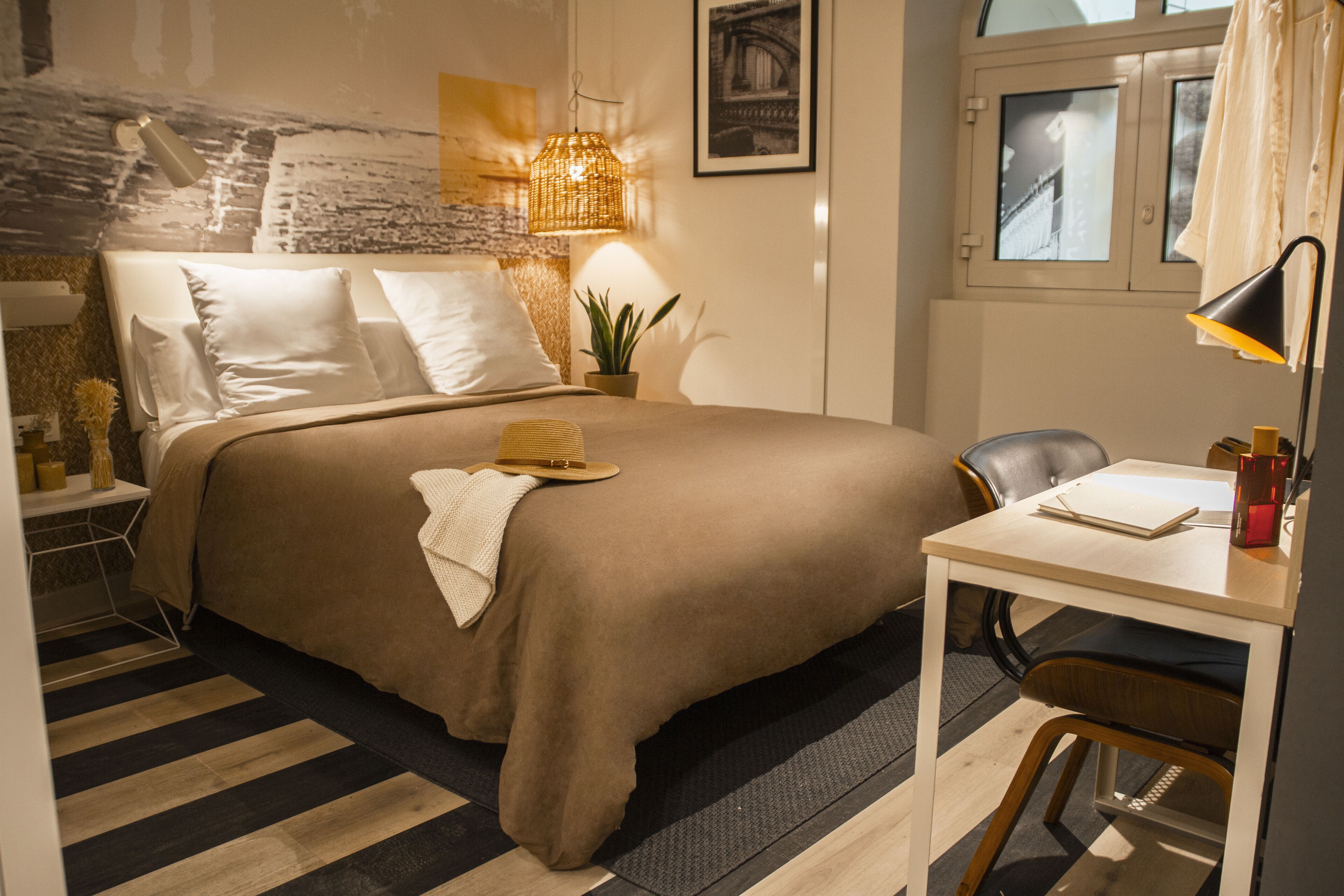 A neatly arranged bedroom with a bed, bedside table, lamp, chair, and a small desk with a chair.