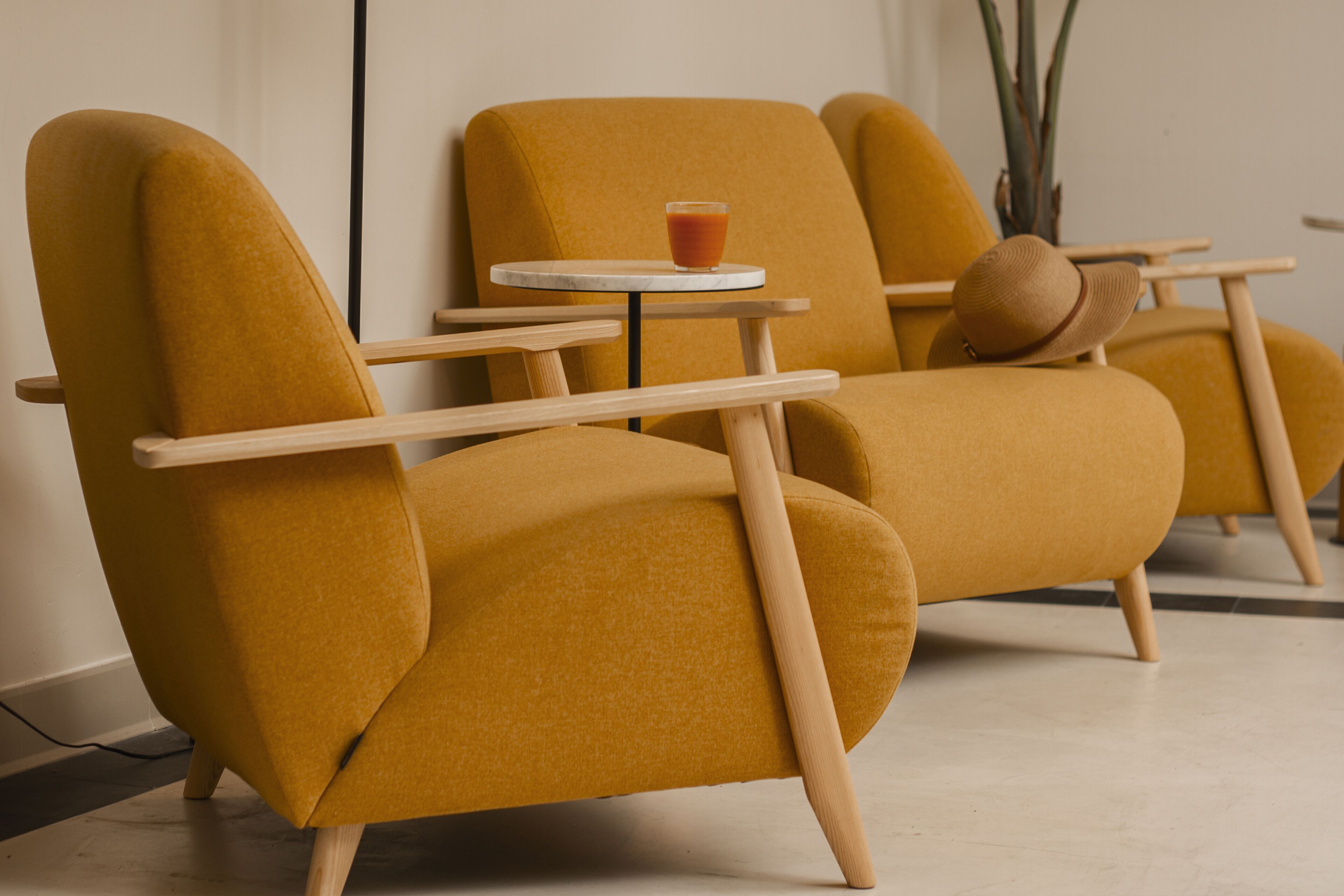 A mustard-colored sofa with wooden armrests and a small table with a glass of orange liquid.