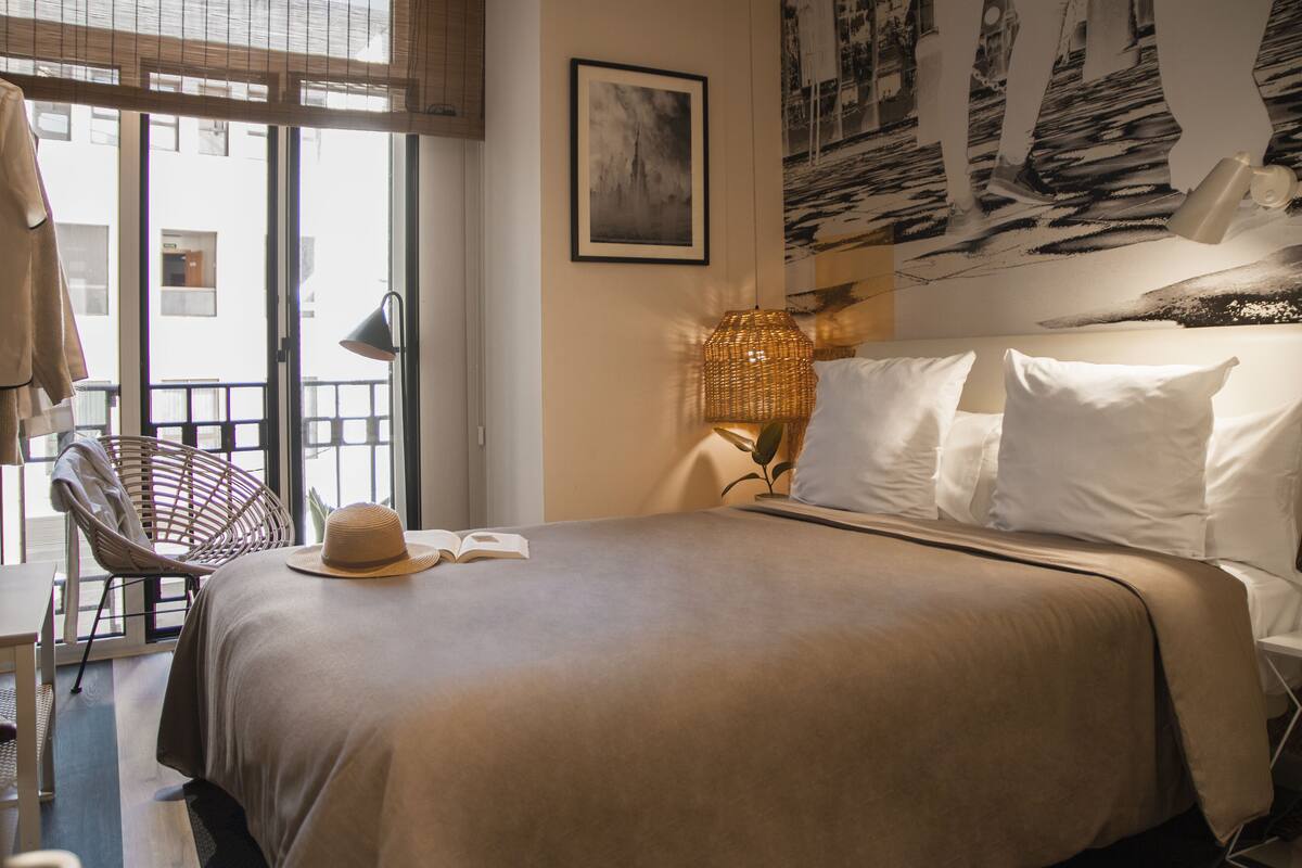 A hotel room with a bed, a chair, a lamp, and a view of the outside.